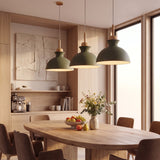 Tres lámparas de diseño colgantes en color verde oliva sobre una mesa de comedor de madera.